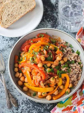 Bowl of Italian Peppers and Chickpeas in front of a plate with two slices of bread and a glass of ice water.