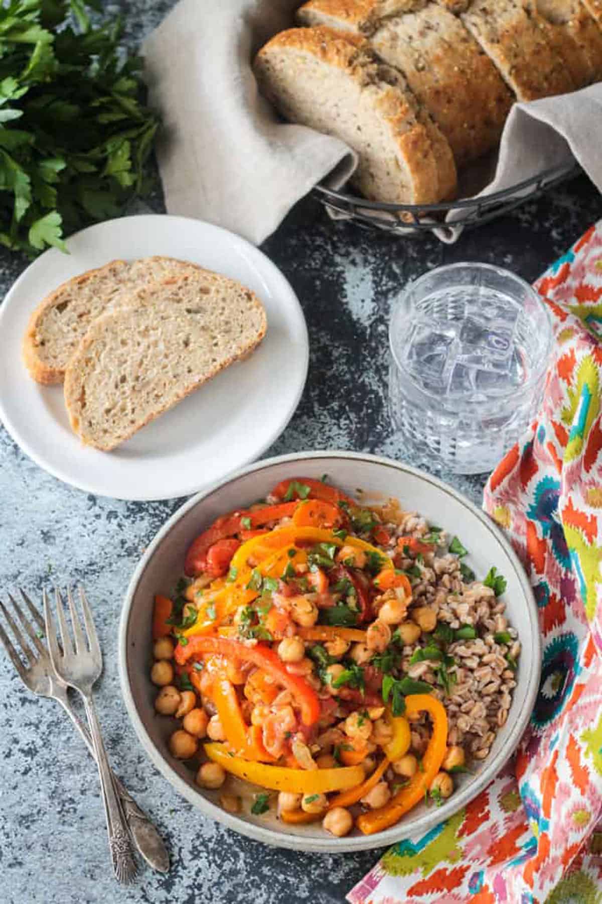 Bowl of Italian Peppers and Chickpeas in front of a plate with two slices of bread and a glass of ice water.