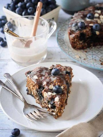 slice of blueberry cake on a plate with two forks in front of a cup of icing