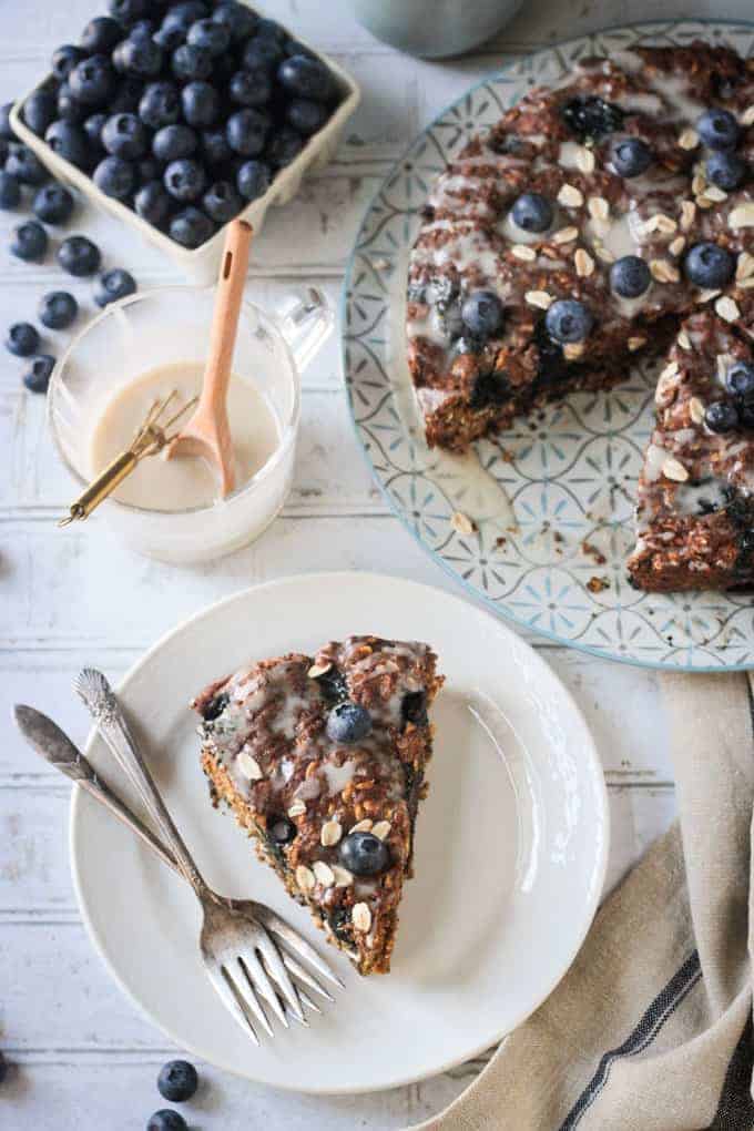 Overhead view of a slice of blueberry breakfast cake in front of the rest of the cake