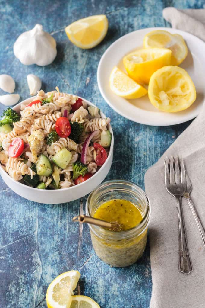 Lemon Dressing in a jar next to a bowl of pasta salad and a plate of lemons.