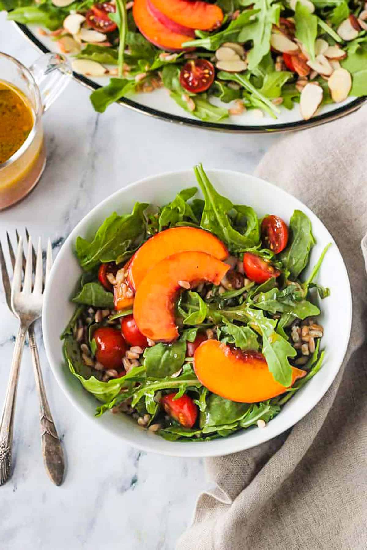 Bowl of arugula peach salad next to two forks.