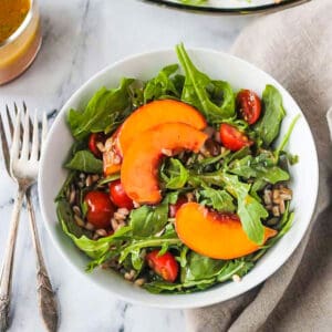 Bowl of arugula peach salad next to two forks.