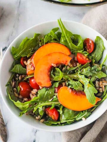 Bowl of arugula peach salad next to two forks.