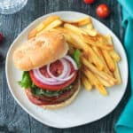 Chickpea veggie burger topped with tomoato and red onion next french fries.