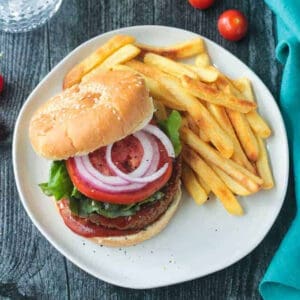 Chickpea veggie burger topped with tomoato and red onion next french fries.