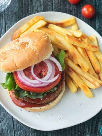 Chickpea veggie burger topped with tomoato and red onion next french fries.