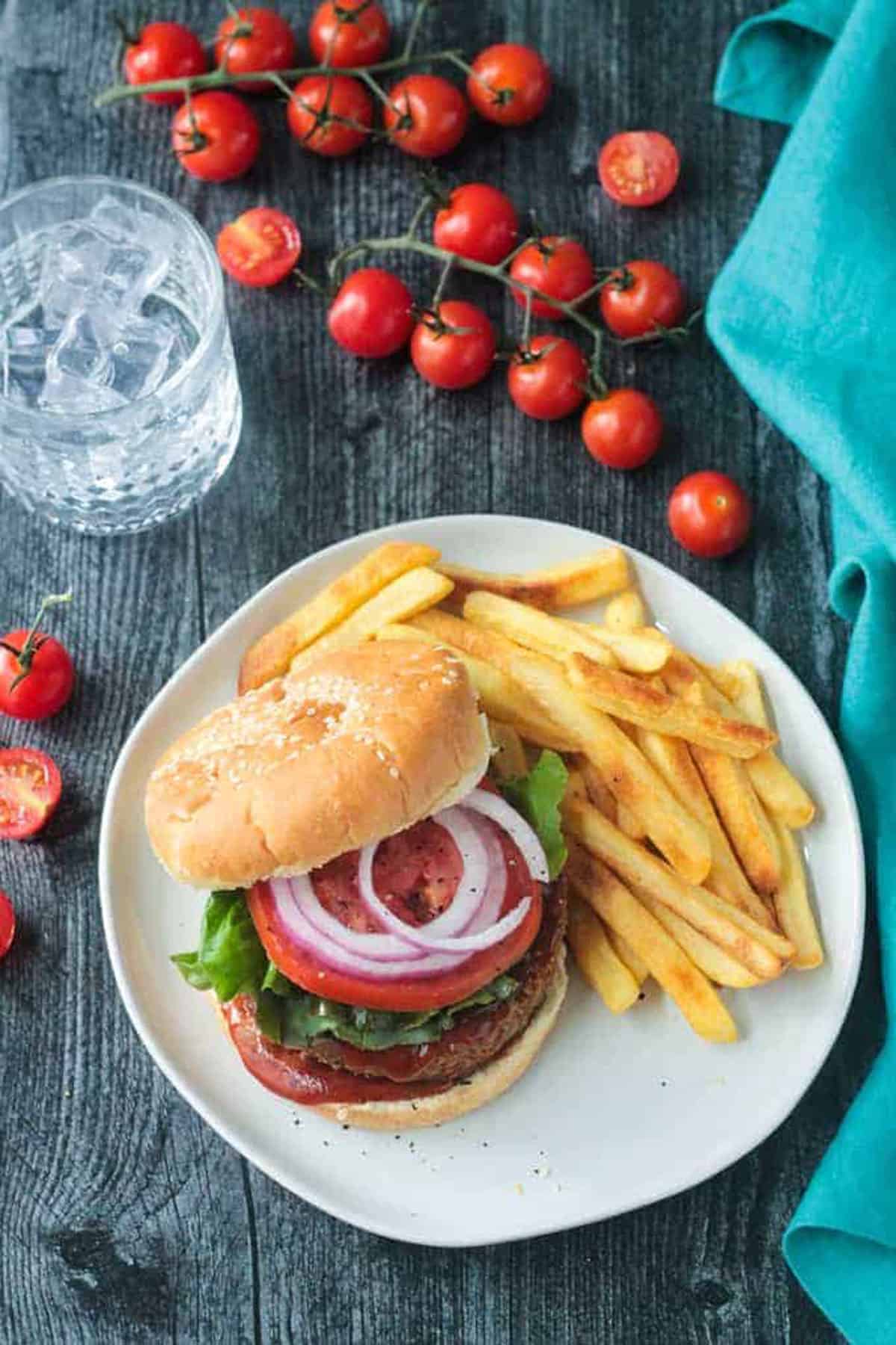 Chickpea veggie burger topped with tomoato and red onion next french fries.