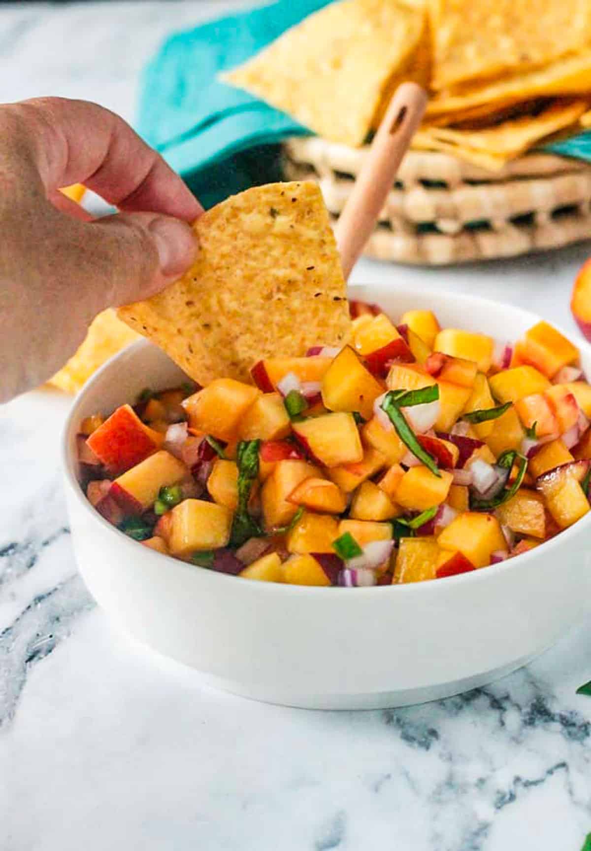 Tortilla chip dipped into a bowl of fresh peach salsa.