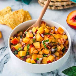 Small wooden spoon in a bowl of peach salsa.
