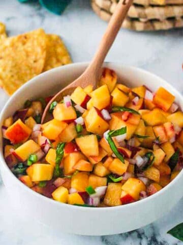 Small wooden spoon in a bowl of peach salsa.