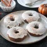Four iced pumpkin donuts on a plate.