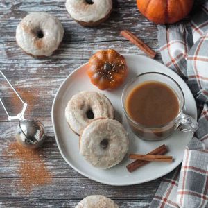 Two white frosted donuts on a plate with a glass mug of coffee and two cinnamon sticks.