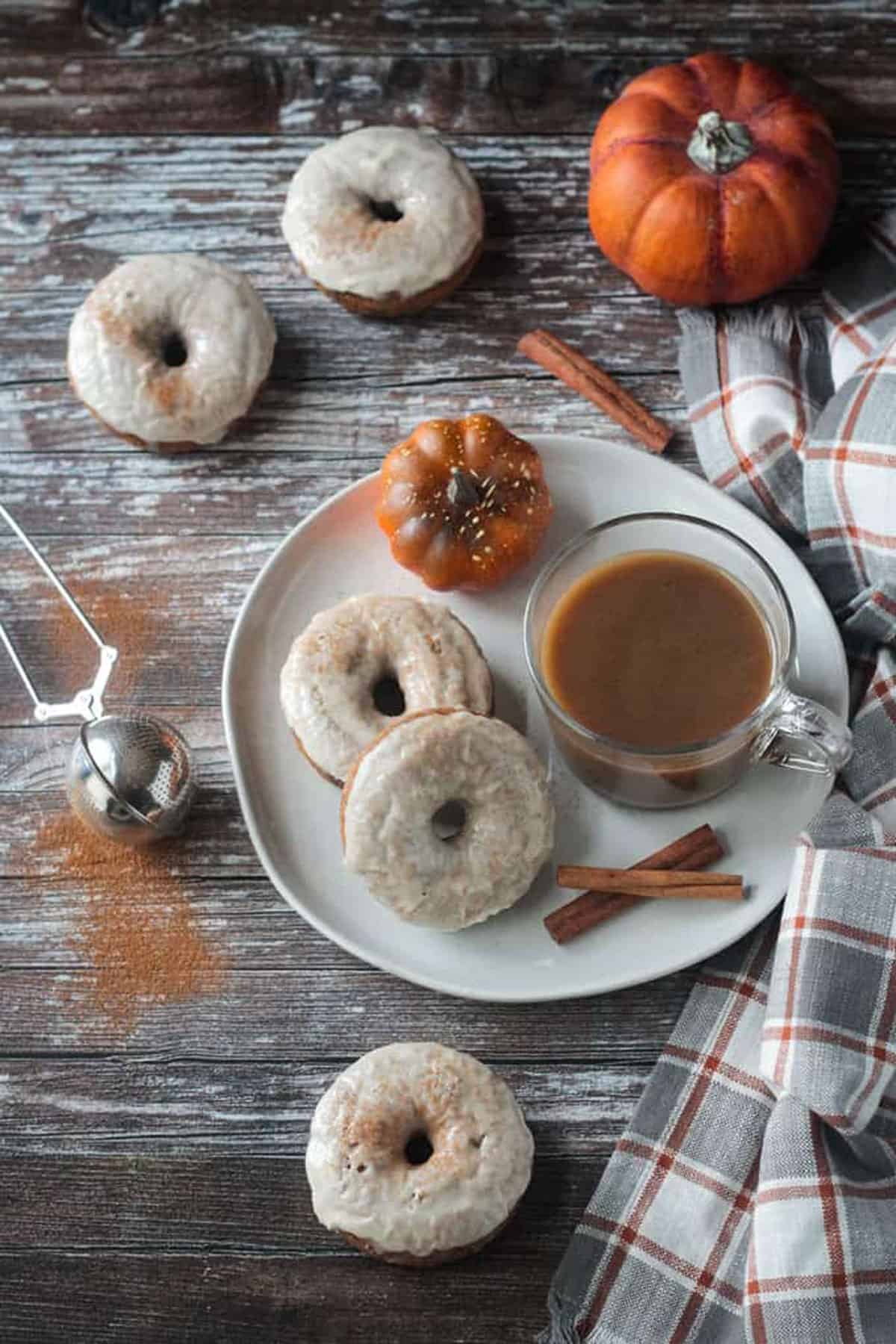 Two white frosted donuts on a plate with a glass mug of coffee and two cinnamon sticks.