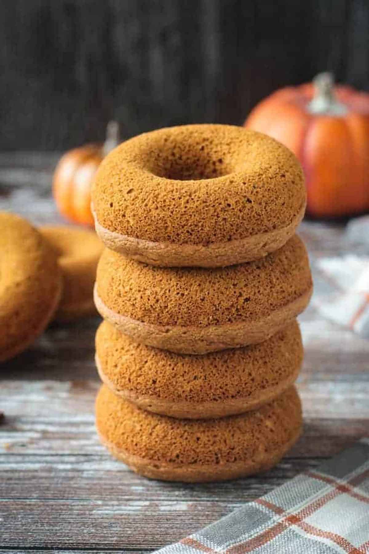 Stack of 4 unfrosted baked vegan pumpkin donuts.