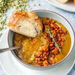 A slice of buttered bread being dunked in a bowl of soup.