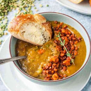 A slice of buttered bread being dunked in a bowl of soup.