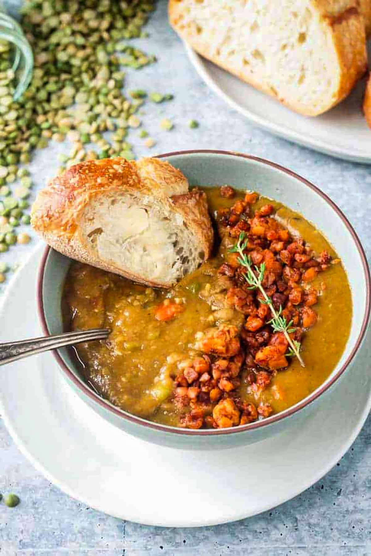 A slice of buttered bread being dunked in a bowl of soup.