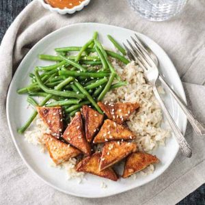 Pan friend tofu in peanut sauce plated with brown rice and green beans.