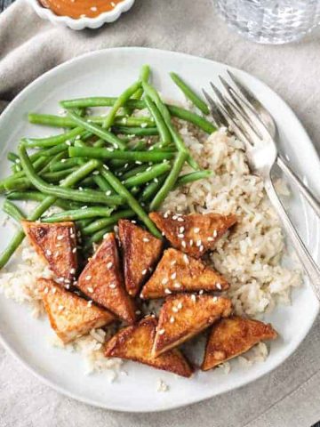 Pan friend tofu in peanut sauce plated with brown rice and green beans.