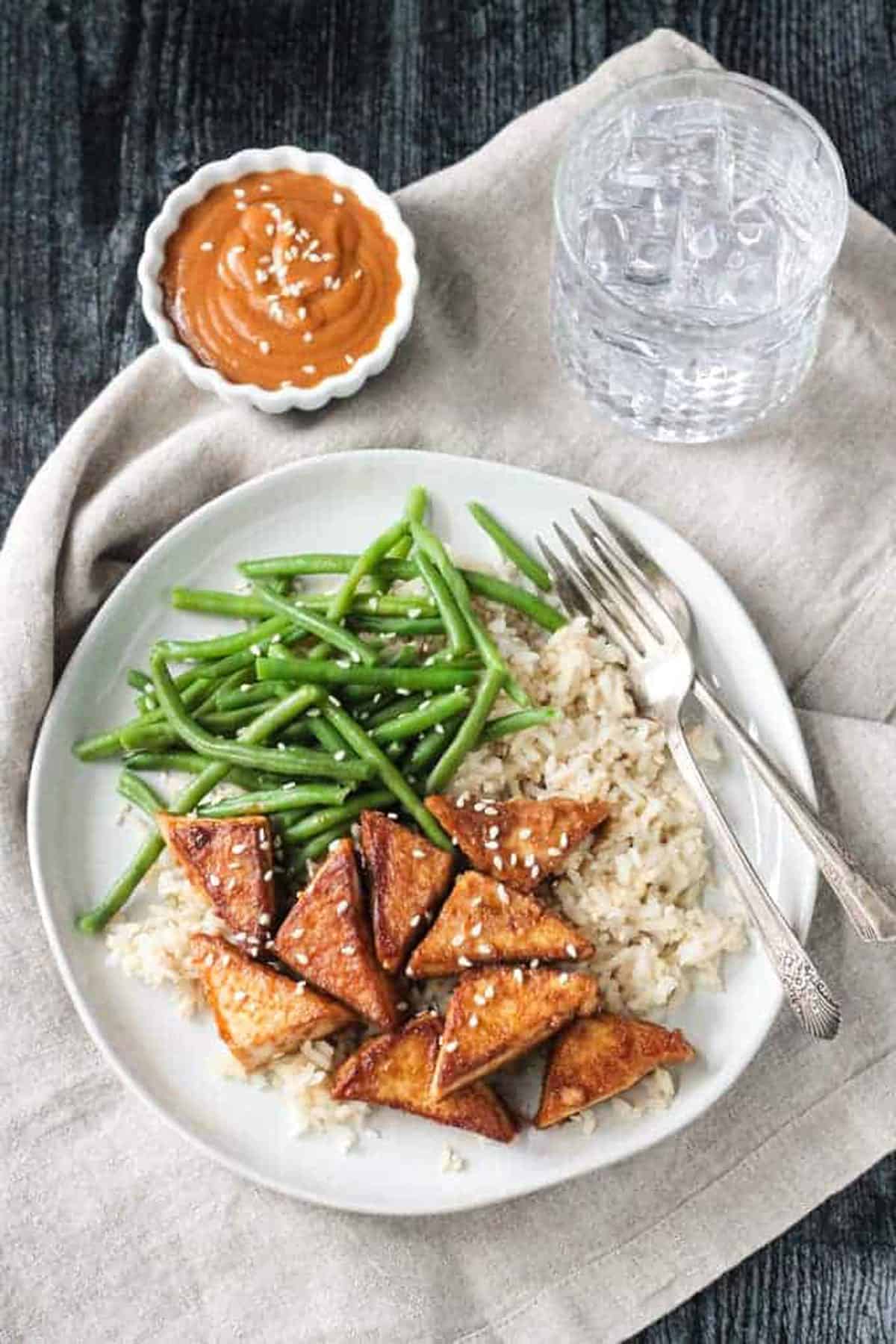 Pan friend tofu in peanut sauce plated with brown rice and green beans.