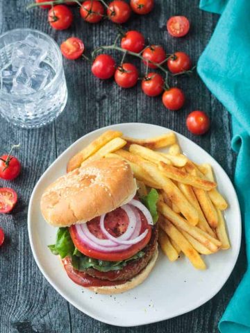 Overhead view of a chickpea veggie burger on a bun with lettuce, tomato, and onion, next to a side of fries.