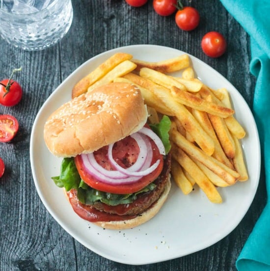 veggie burger on a bun with tomato, lettuce, red onion and bbq sauce next to a side of french fries