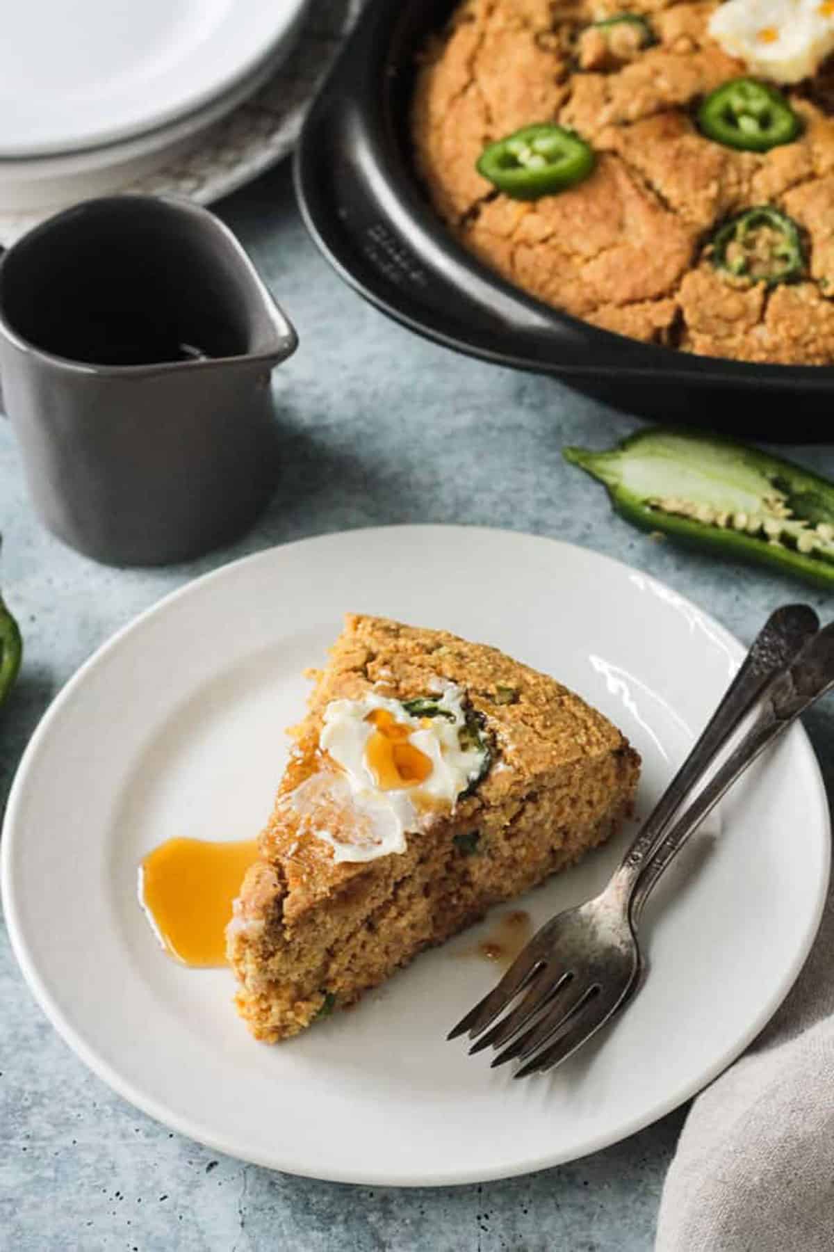 One slice of vegan jalapeño cornbread topped with butter and maple syrup.