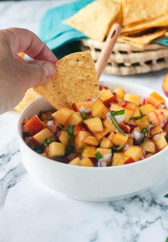 Tortilla chip dipping into a bowl of peach salsa