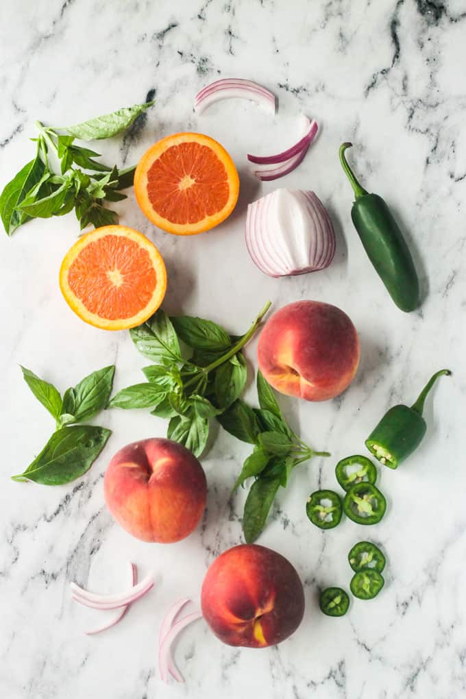 Individual ingredients for peach salsa laid out on a marble slab