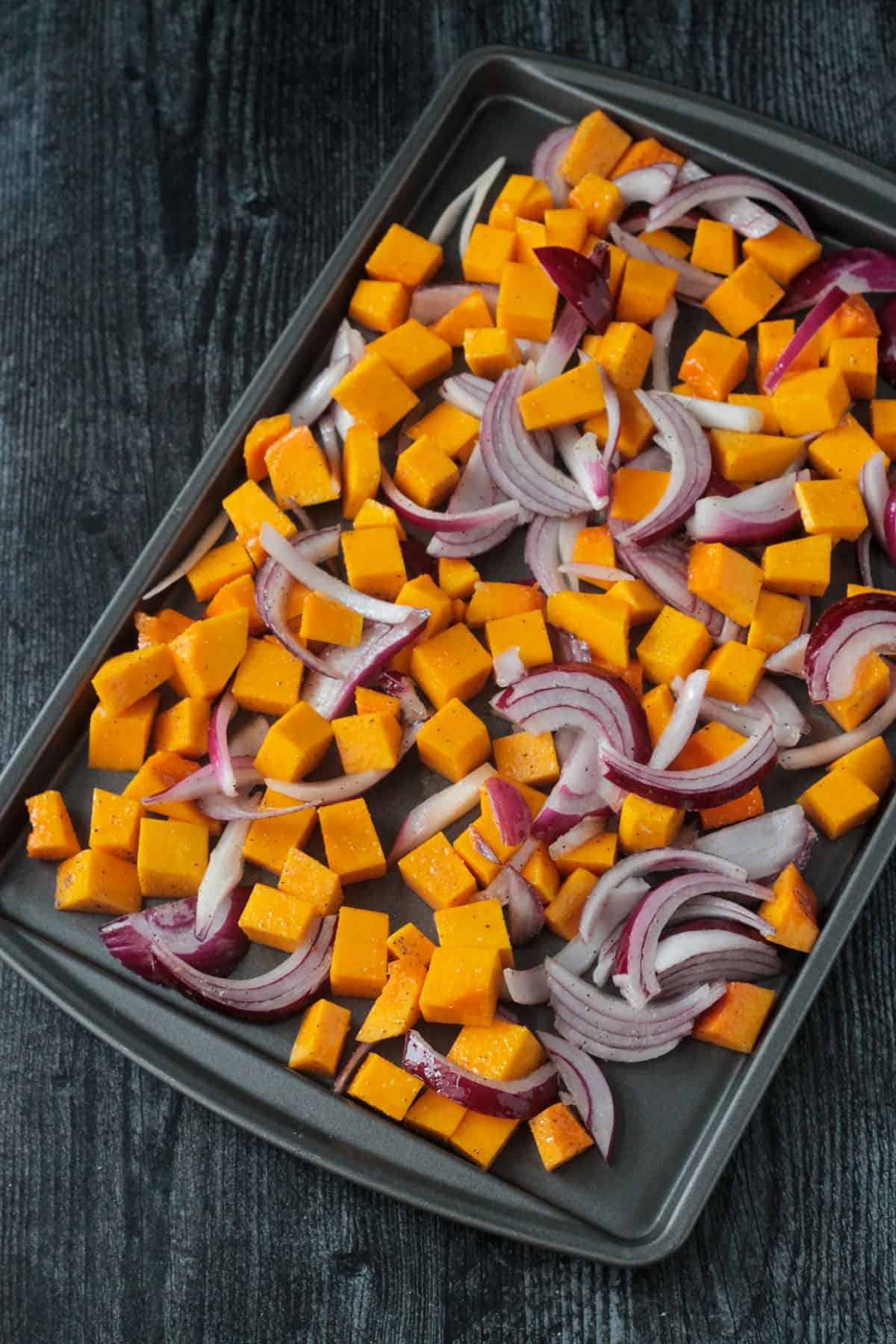 Chopped butternut squash and sliced red onions on a baking sheet.