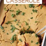 A scoop of cornbread casserole being lifted out of the baking dish.