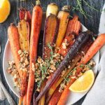 Plate of orange thyme rainbow roasted carrots topped with toasted walnuts .