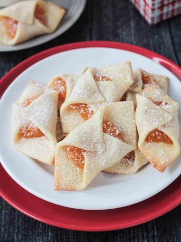 Close up view of a plate of kolaczki cookies filled with apricot jam and dusted with powdered sugar