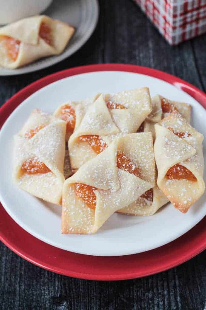 Close up view of a plate of kolaczki cookies filled with apricot jam and dusted with powdered sugar