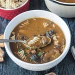 Spoonful of mushroom soup with rotini noodles being lifted out of a bowl.