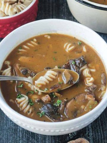 Spoonful of mushroom soup with rotini noodles being lifted out of a bowl.