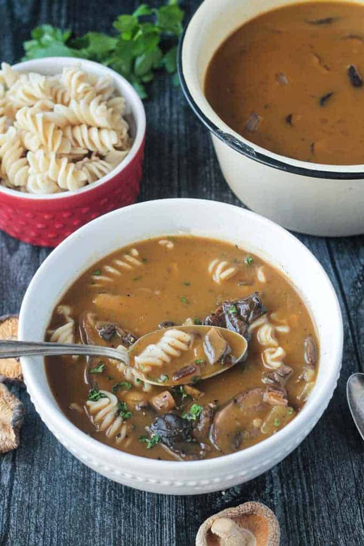 Spoonful of mushroom soup with rotini noodles being lifted out of a bowl.