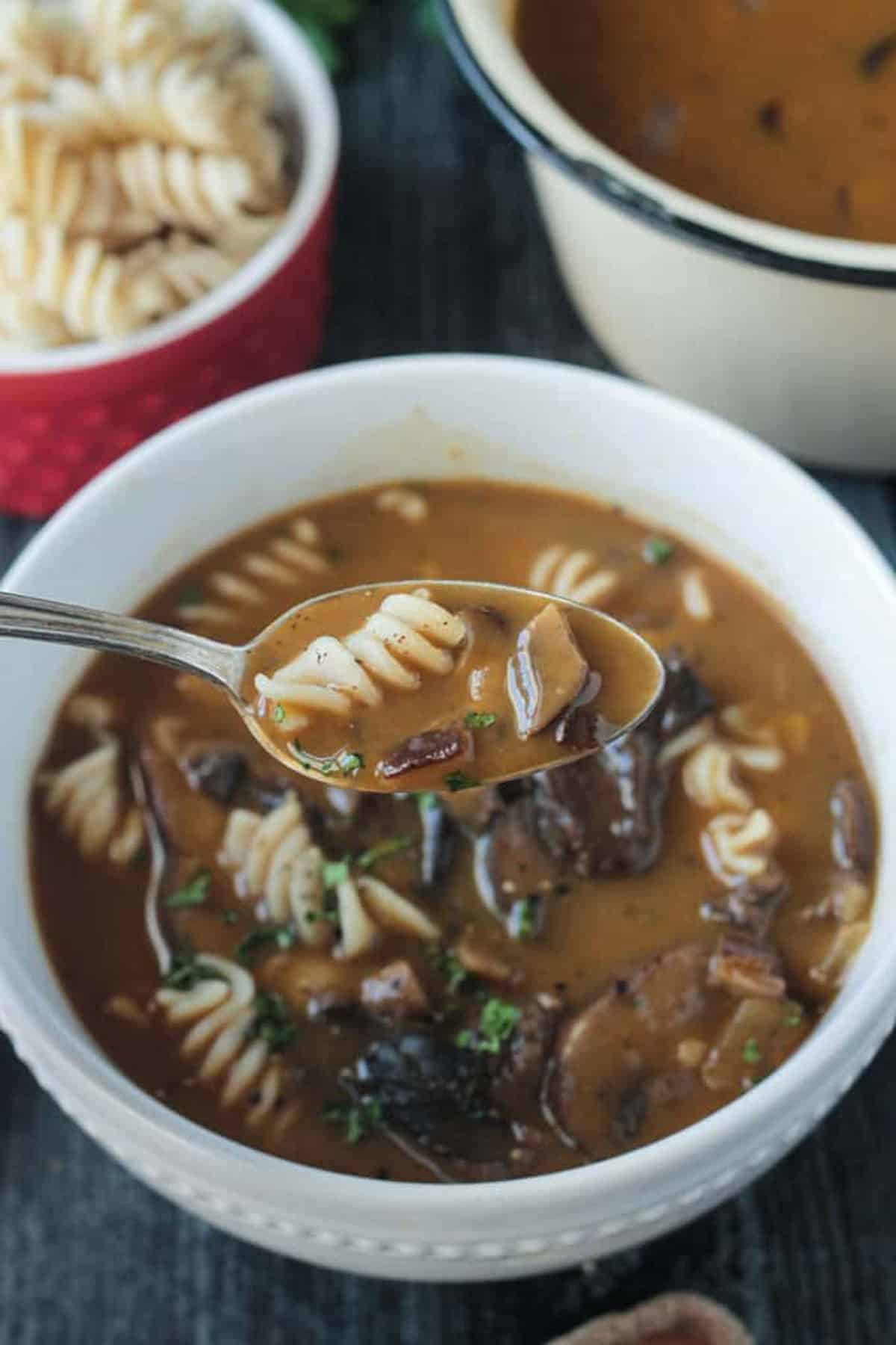 Close up of a sliced mushroom and rotini noodle on a spoon with broth.