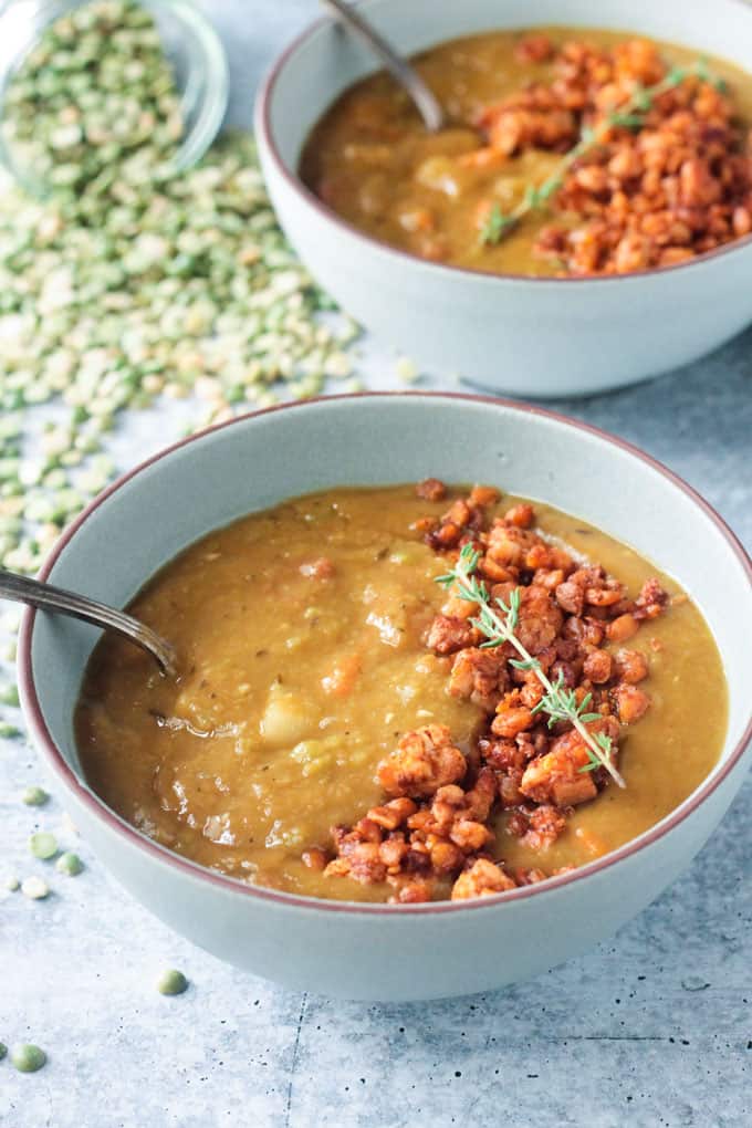 Spring of fresh thyme lying across crumbled tempeh in a bowl of vegan split pea soup