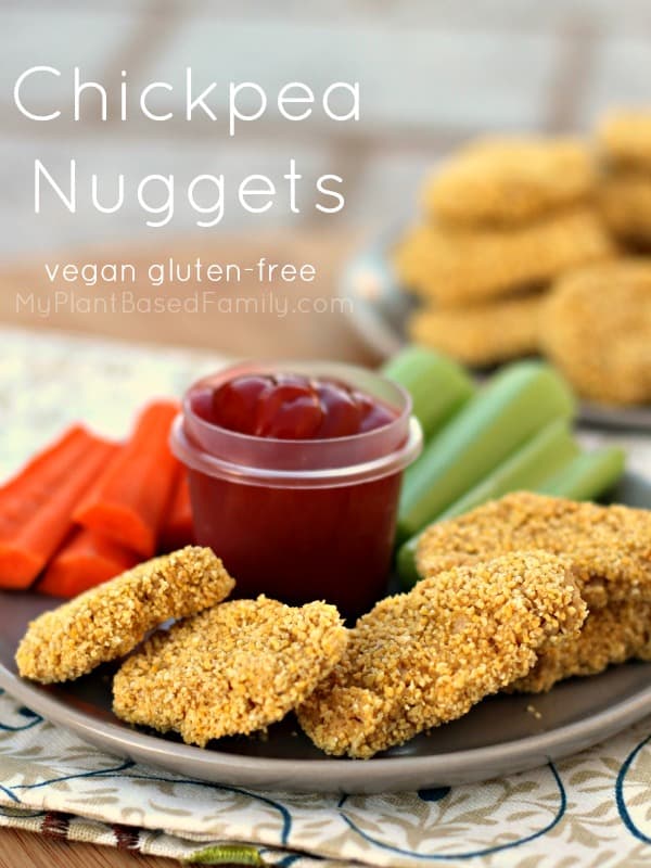 chickpea nuggets lined up on a plate with ketchup and sliced vegetables