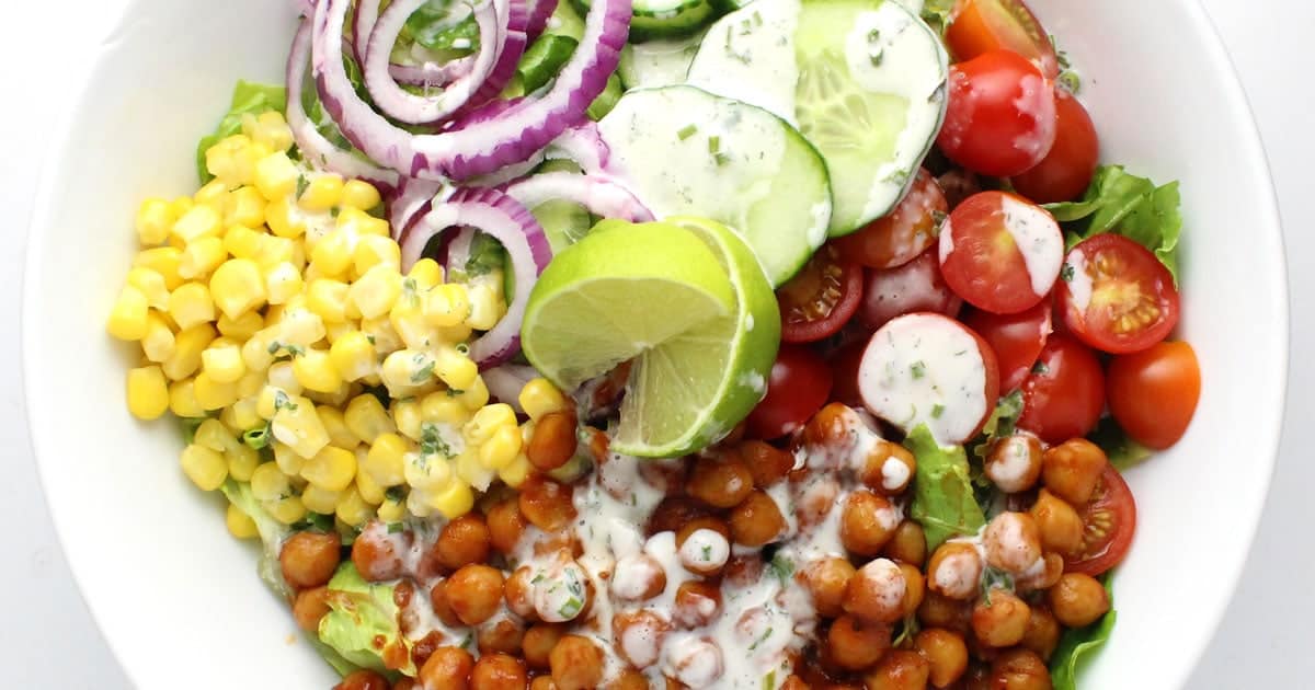bowl of corn, chickpeas, tomatoes, cucumber, and red onion drizzled in a white sauce