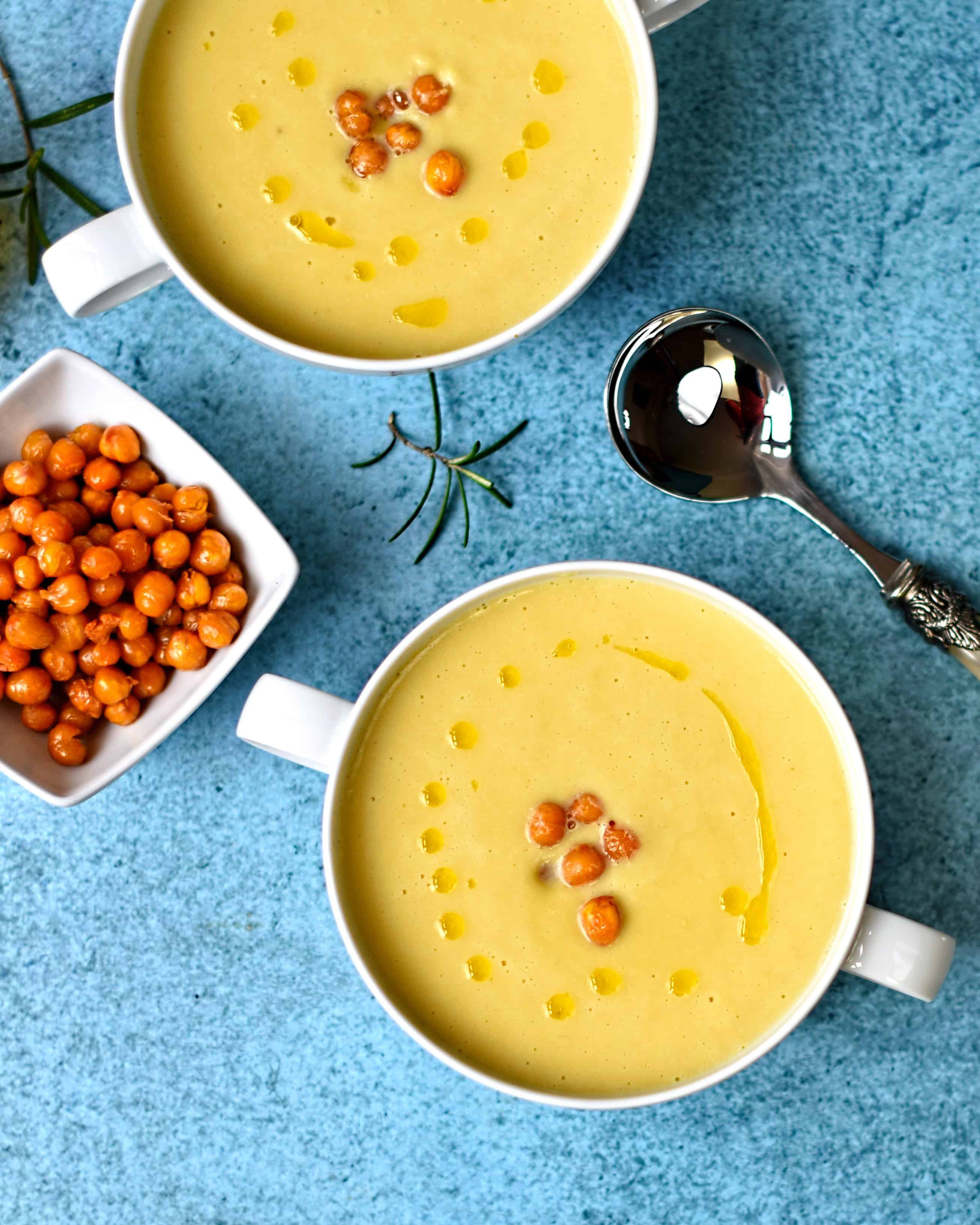 two bowls of yellow soup garnished with chickpeas in the center