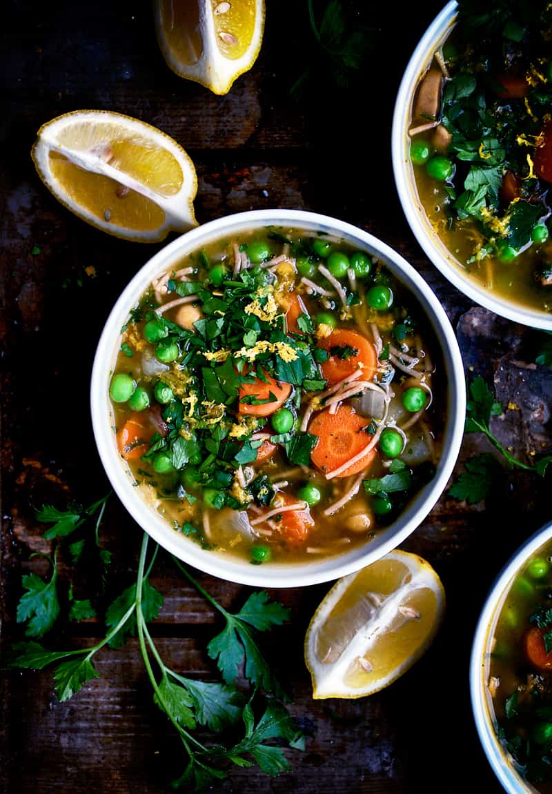 lots of veggies in a bowl of soup with lemon wedges nearby