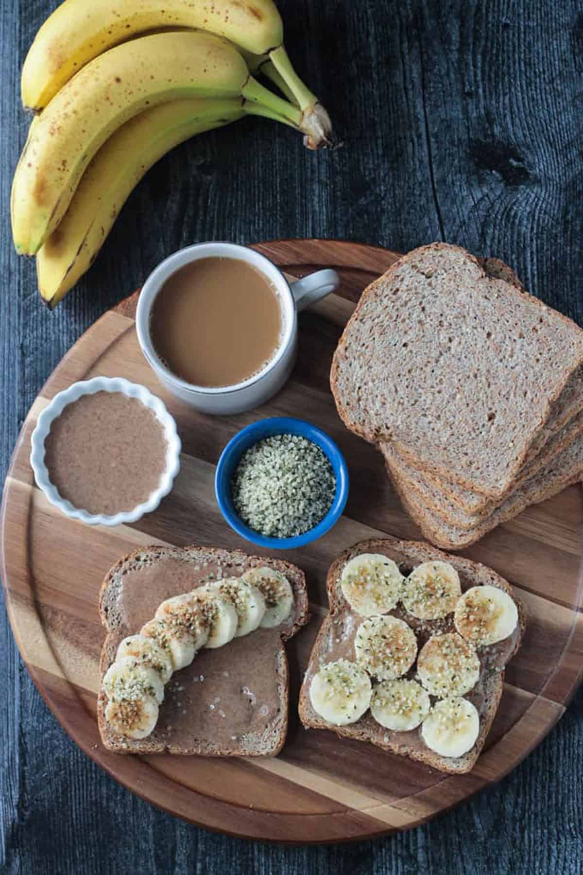 Bread, bananas, hemp seeds, coffee, and almond butter all laid out on a wooden platter.