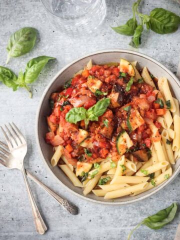 Two forks lying next to a plate of pasta.