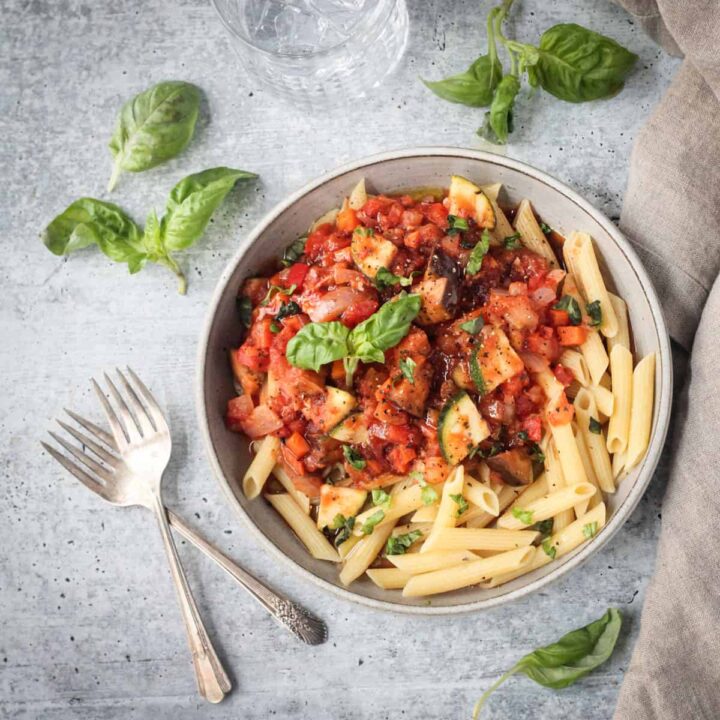 Two forks lying next to a plate of pasta.