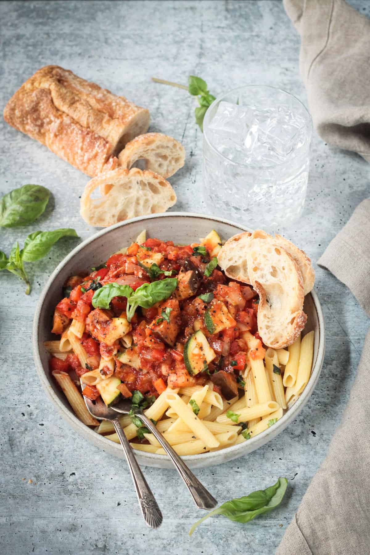 fork in a bowl of veggie pasta next to a loaf of crusty bread