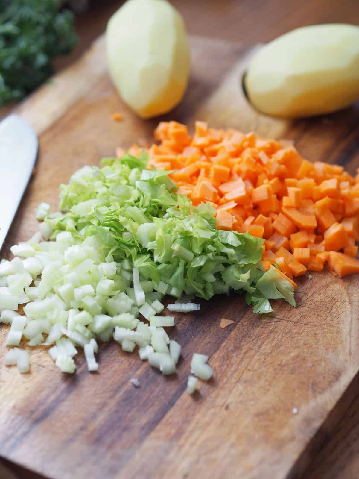 Diced onion, celery, and carrot on a wooden cutting board.
