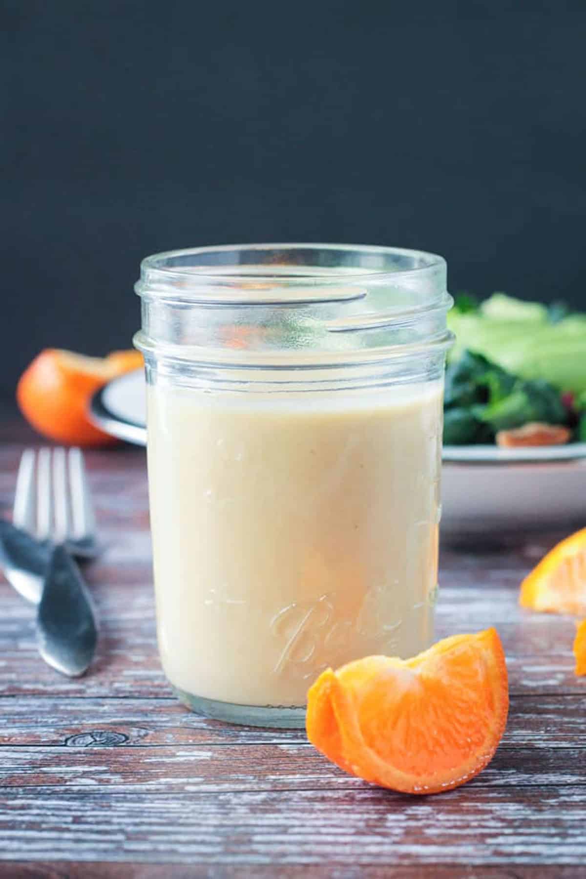One orange wedge on a table in front of a glass jar of salad dressing.